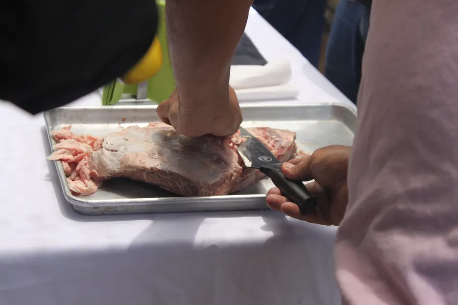 Corte técnico de un costillar con cuchillo de chef sobre charola metálica